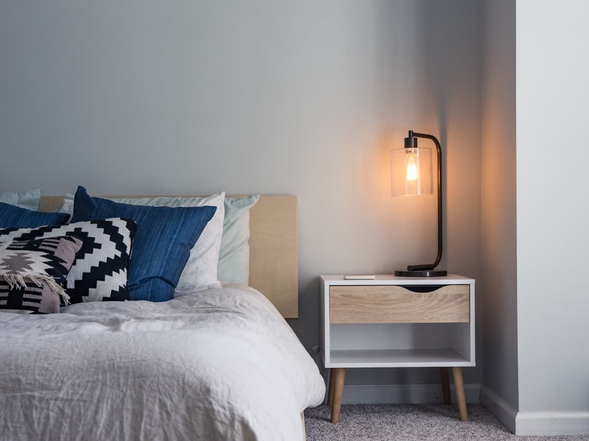 Soft pillows resting on a bed beside a warm bedside lamp